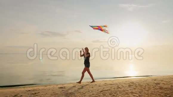 无忧无虑的年轻女人带着风筝在海滩上奔跑在美丽的日落天空的背景下视频的预览图