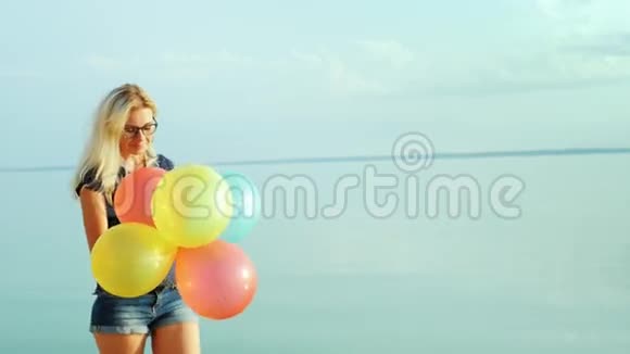 蓝天背景下一位无忧无虑带着气球在海上行走的年轻女子的肖像视频的预览图