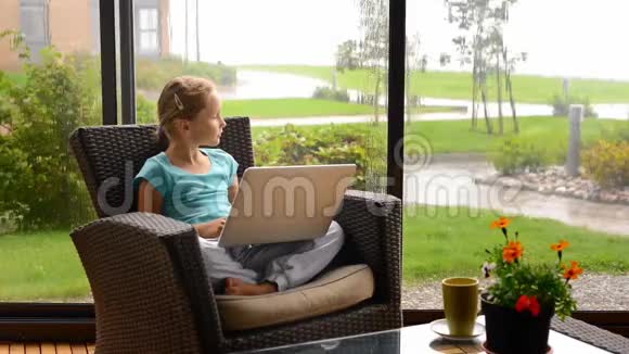 小女孩坐在露台上坐在扶手椅上手提电脑视频的预览图