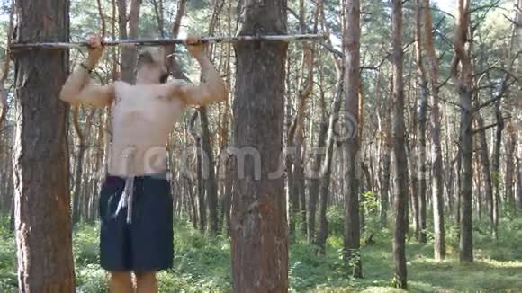 强壮的肌肉男在森林里做拉力运动年轻的运动员在木头的水平杆上做下巴健身视频的预览图