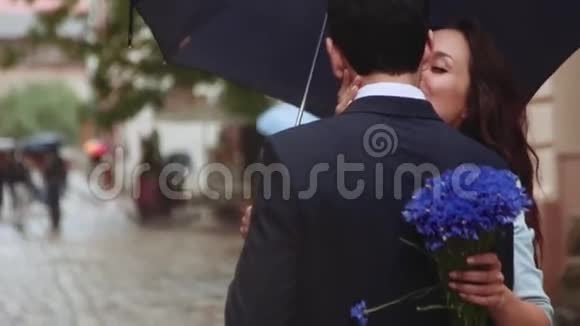 很少有一对漂亮的年轻夫妇在伞下迷人的女孩正在拥抱和亲吻她的男朋友女孩视频的预览图