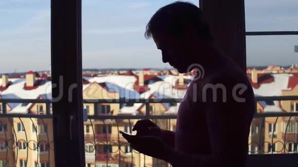 一个男人在他的智能手机上滚动应用程序的剪影靠近大窗口4K近距离射击视频的预览图