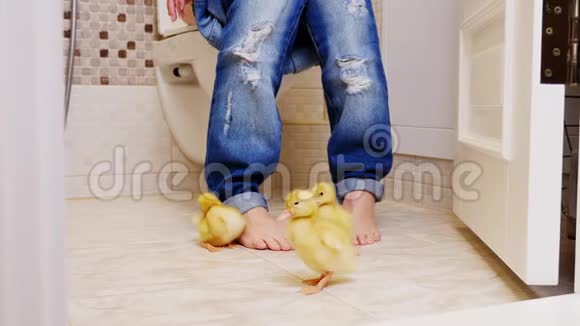 厕所厕所里女孩坐在厕所里你可以看到她穿牛仔裤的腿她赤脚在她旁边在视频的预览图