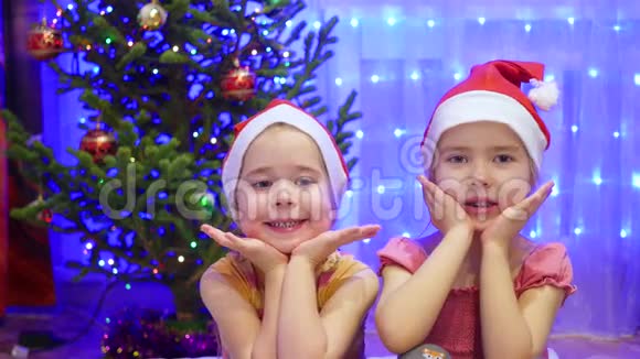两个迷人的女孩在圣诞节的晚上微笑和跳舞在圣诞节的背景灯光和花环视频的预览图