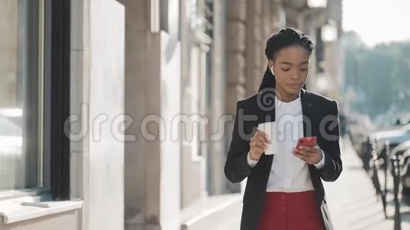 一位年轻的非洲裔美国女商人穿着西装在城市里走来走去喝着咖啡用着视频的预览图