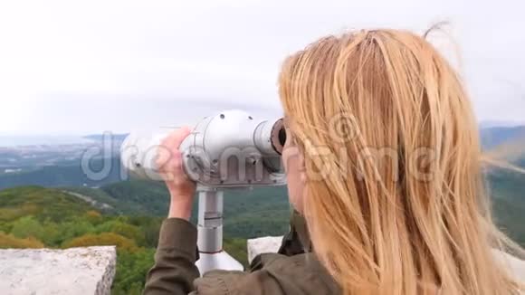 一个金发女郎透过山顶上的望远镜看4k慢镜头视频的预览图