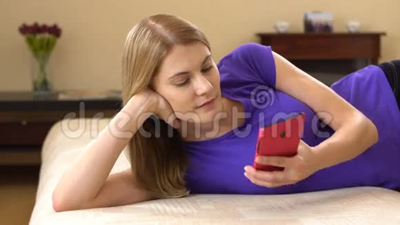 美丽迷人的年轻女子穿着紫罗兰色的t恤躺在沙发上打着电话视频的预览图