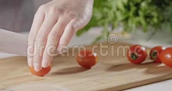 穿着围裙的女人把红樱桃西红柿切成两半用刀切在木板上准备沙拉视频的预览图