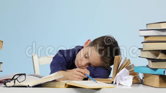 疲惫的男孩在书间的一张桌子上睡着了蓝色背景视频的预览图