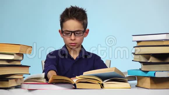 疲倦的男孩坐在桌子旁看书睡着了醒来蓝色背景视频的预览图