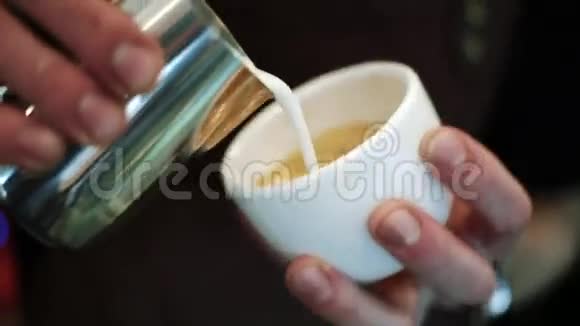 咖啡师把牛奶倒入一杯浓咖啡中混合成卡布奇诺在牛奶泡沫上涂上油漆视频的预览图