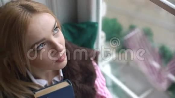 特写一个美丽的女孩的肖像有一本书看着窗外和镜头视频的预览图
