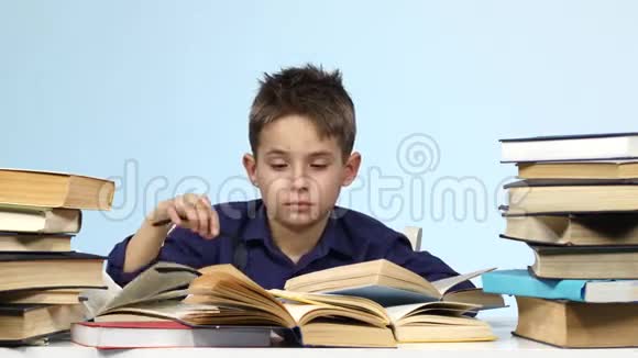 昏昏欲睡的小男孩坐在桌子旁疲惫不堪地翻阅着一本书蓝色背景视频的预览图