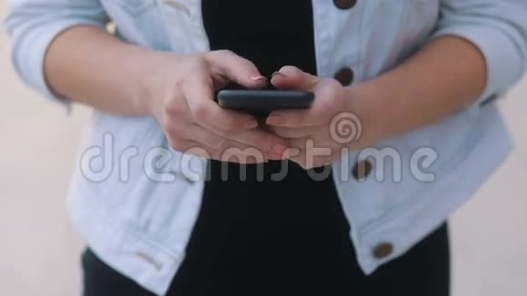 穿着白色牛仔裤外套和黑色t恤的年轻温柔女孩的特写镜头与智能手机Stadicam慢动作交流视频的预览图