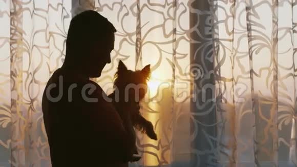 一个年轻的单身男子站在窗口抱着他的狗视频的预览图