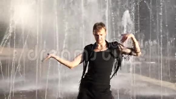 一个年轻快乐的家伙跳着现代芭蕾在一个夏天公园的喷泉的背景下摇摇晃晃缓行视频的预览图