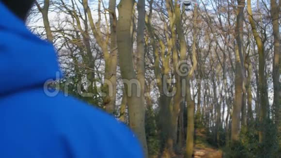 一个穿着蓝色夹克的人正带着无人机在森林里飞行视频的预览图