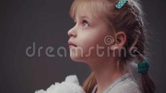 可爱的金发女婴一双蓝色的大眼睛抱着她最喜欢的玩具白色泰迪熊看着远处然后转过身来视频的预览图