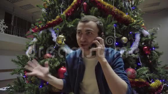 智能手机人在圣诞树背景下打手机视频的预览图