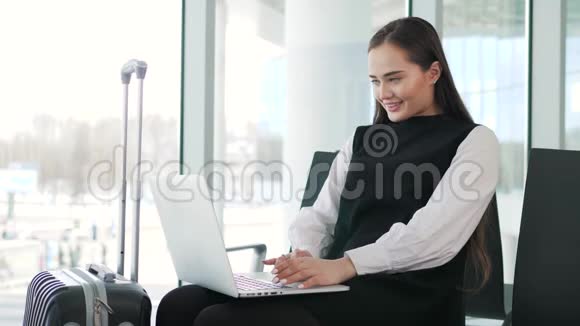 机场年轻女乘客在候机大厅坐着智能手机和笔记本电脑等待她的航班工作视频的预览图