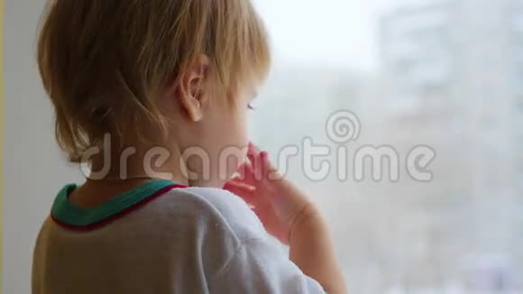 一个孩子站在窗台上看着窗外的特写镜头视频的预览图
