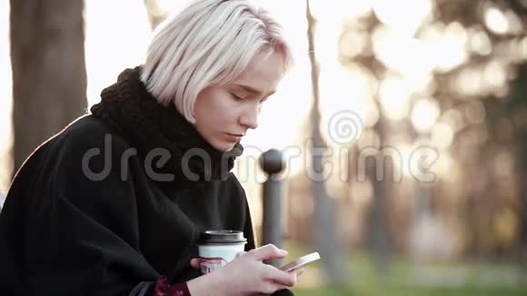 在外面的金发女孩手里拿着智能手机和咖啡悲伤地在智能手机上读着这条信息视频的预览图