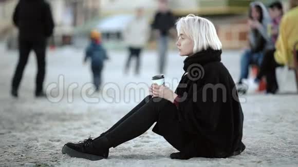 外面的金发女孩在海滩上她喝咖啡享受海风坐在白沙上视频的预览图