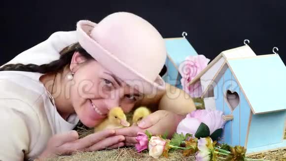 肖像一个漂亮的年轻女人有两条辫子戴着一顶有趣的粉红色帽子和小黄鸭玩耍工作室视频的预览图