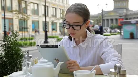 优雅的商务女士喝着咖啡思考着看着街上一家自助餐厅里的平板电脑视频的预览图