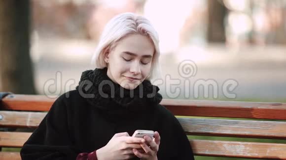 外面的金发女孩看着智能手机坐在长凳上拨通智能手机里的文字微笑着视频的预览图