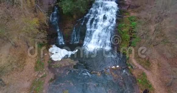 空中镜头飞过美丽的瀑布有苔藓绿草森林树木和岩石乌克兰视频的预览图