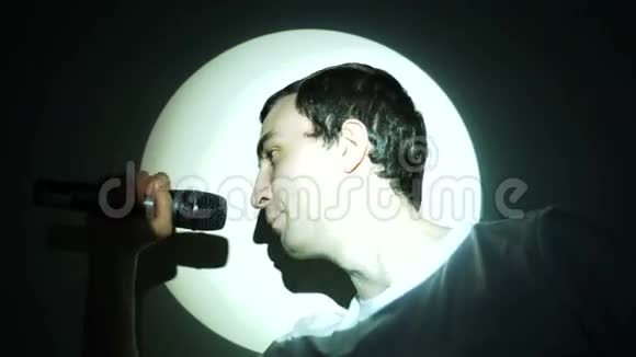 一个年轻人在白光束中对着麦克风唱歌视频的预览图