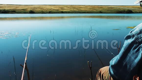 渔夫在湖岸的钓竿上钓鱼光滑美观的水面渔夫在等视频的预览图