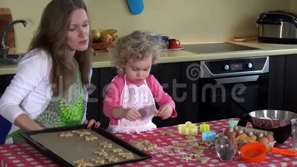 可爱的母女把饼干放进厨房的烤盘里视频的预览图