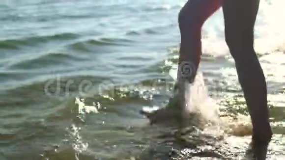 一个美丽的年轻女孩在海滩和天空的背景下脚站在水中溅起水花的肖像视频的预览图