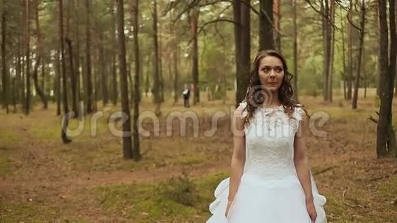 在新鲜空气中的森林里快乐的一对新郎带着一束美丽的花向新娘走去新娘一动不动地站着视频的预览图