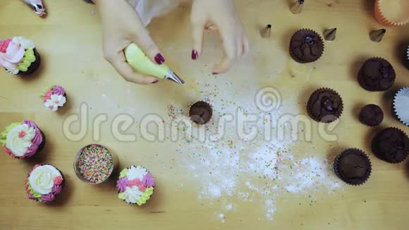 女性手装饰巧克力纸杯蛋糕的俯视图年轻女人用糕点包做奶油视频的预览图