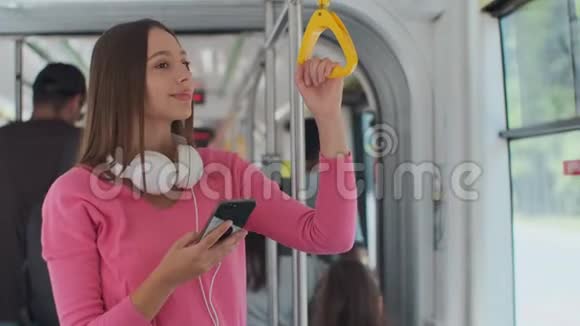 年轻女性乘客在公共交通工具上享受旅行站在现代有轨电车上的智能手机视频的预览图