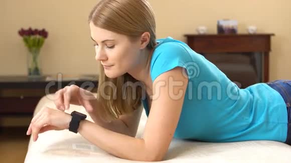 美丽迷人的年轻女人躺在沙发上在她的智能手表上口述一条信息视频的预览图