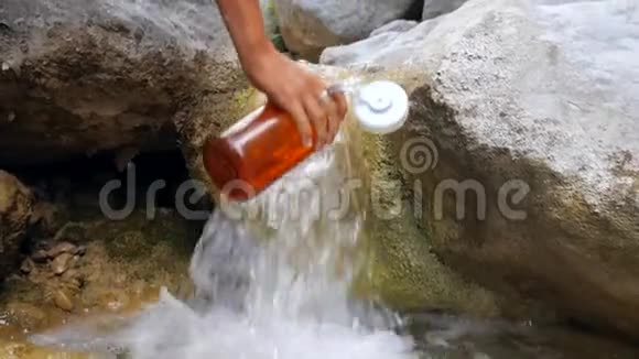 徒步旅行者的女人从森林中的瀑布把清澈的水收集到瓶子里高清慢镜头视频的预览图