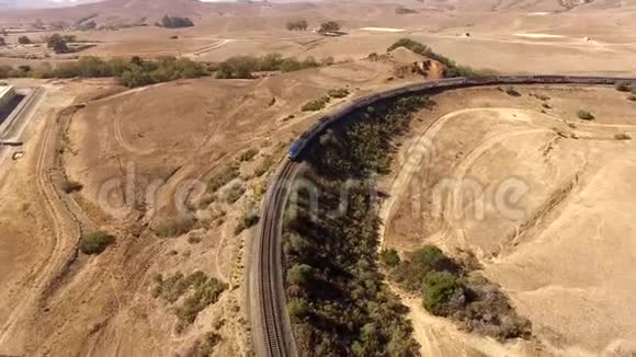 现代城市客运列车在草原峡谷山景观中穿越巨大干沙沙漠的4k空中无人机射击视频的预览图
