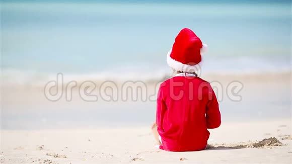 圣诞节假期在白色海滩上戴圣诞帽的可爱女孩的后景视频的预览图