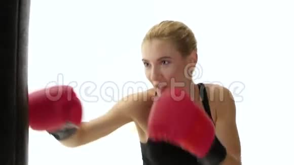 一个肌肉发达的金发女拳击手哭喊着踢着拳击袋视频的预览图
