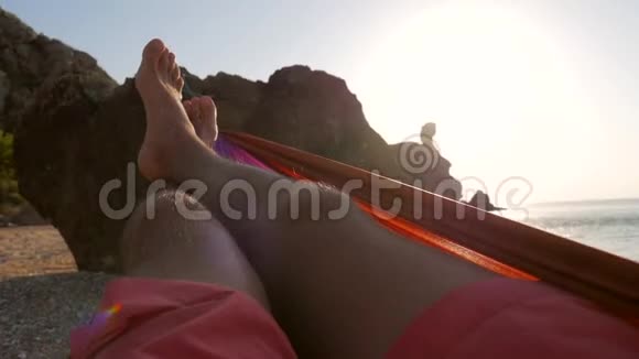 在日落时分双脚在海边的吊床上摆动美丽夕阳剪影暖色调慢动作视频的预览图