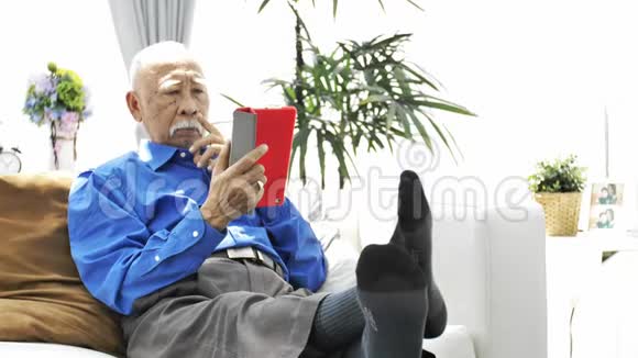 带着白胡子的亚洲老人在家里用平板电脑视频的预览图