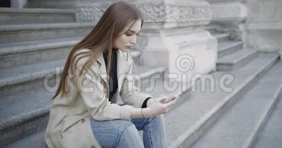女人坐在楼梯上用智能手机视频的预览图