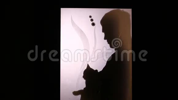 一个男人的剪影在玻璃门后面他把猫抱在怀里抚摸它宠物视频的预览图