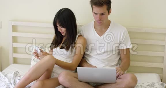 年轻的情侣坐在床上手提电脑视频的预览图
