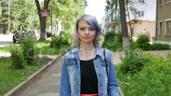 年轻的金发女孩有着专业的化妆和发型蓝色的头发穿着黑色的连衣裙沿着的道路去寻找相机视频的预览图