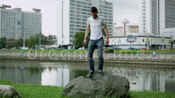 穿牛仔裤和蓝色t恤的留胡子的家伙正从岩石上跳下来视频的预览图